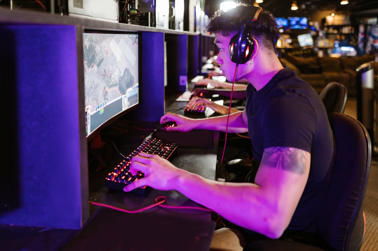 A focused gamer plays on a high-performance PC in a modern cyber café setting under purple lighting.