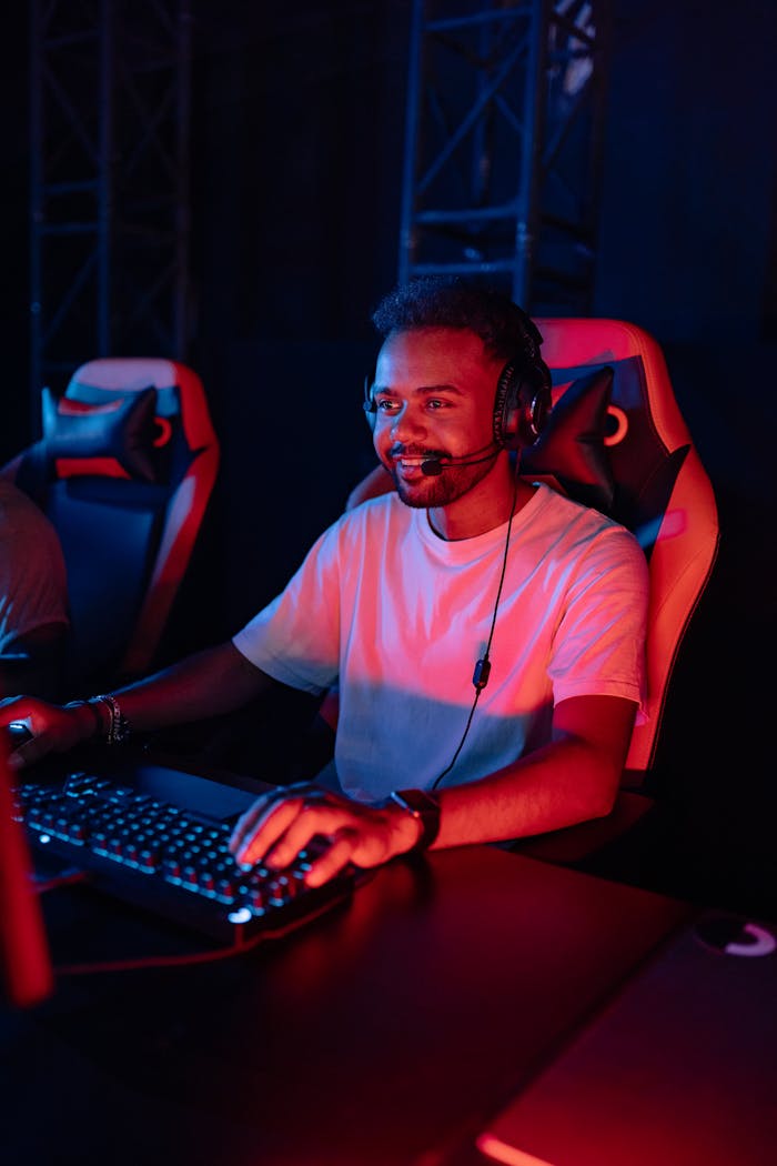 An African American man engaged in gaming at a computer station, wearing a headset.